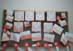 Na tablicy przypięte prace: flagi, kokardy biało-czerwone i pokolorowane godła Polski.